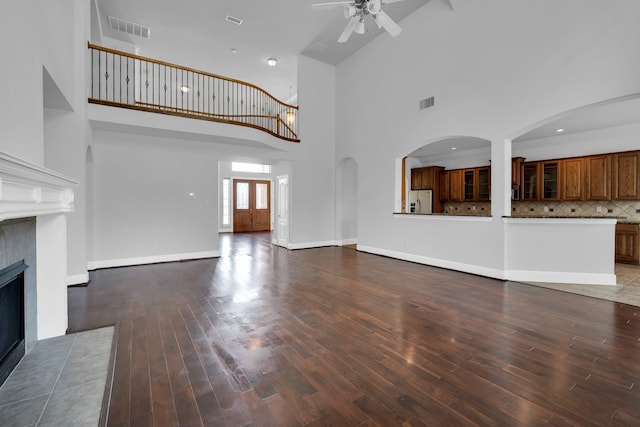 unfurnished living room with a tile fireplace, ceiling fan, a high ceiling, and hardwood / wood-style flooring