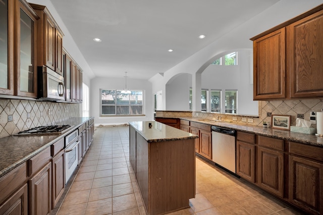 kitchen with decorative backsplash, appliances with stainless steel finishes, decorative light fixtures, a kitchen island, and lofted ceiling