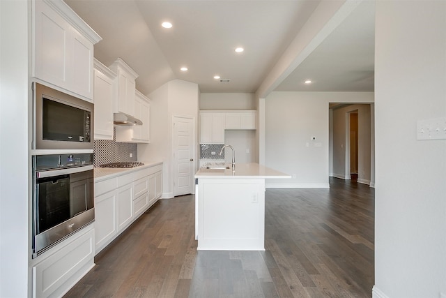 kitchen featuring decorative backsplash, white cabinetry, dark wood-type flooring, stainless steel appliances, and a center island with sink