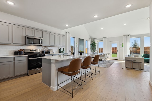 kitchen featuring appliances with stainless steel finishes, a kitchen island with sink, a kitchen breakfast bar, and light hardwood / wood-style flooring