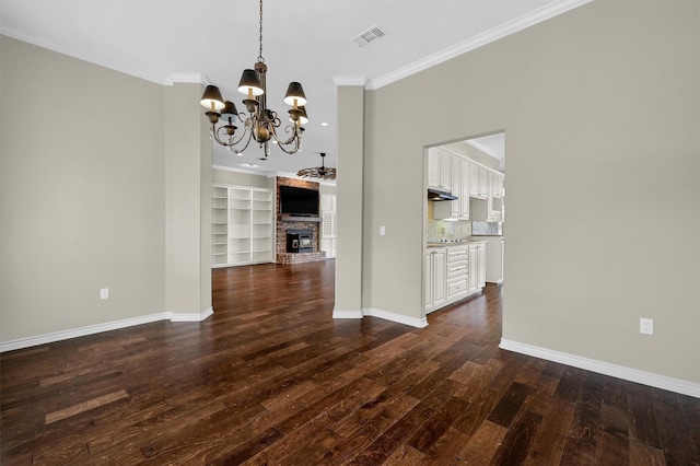 unfurnished dining area featuring dark hardwood / wood-style flooring, a notable chandelier, crown molding, and a fireplace