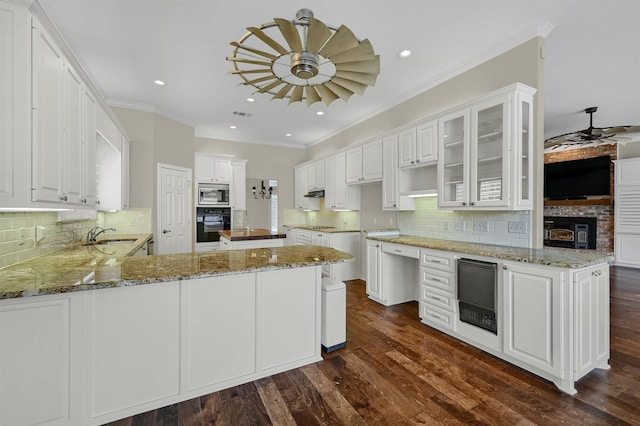 kitchen with black oven, stone counters, stainless steel microwave, white cabinets, and kitchen peninsula