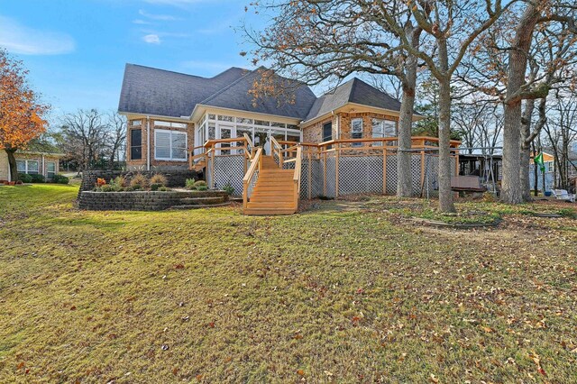 rear view of house with a sunroom, a deck, and a lawn