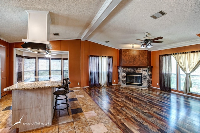 kitchen featuring a stone fireplace, a breakfast bar, lofted ceiling with beams, crown molding, and light wood-type flooring