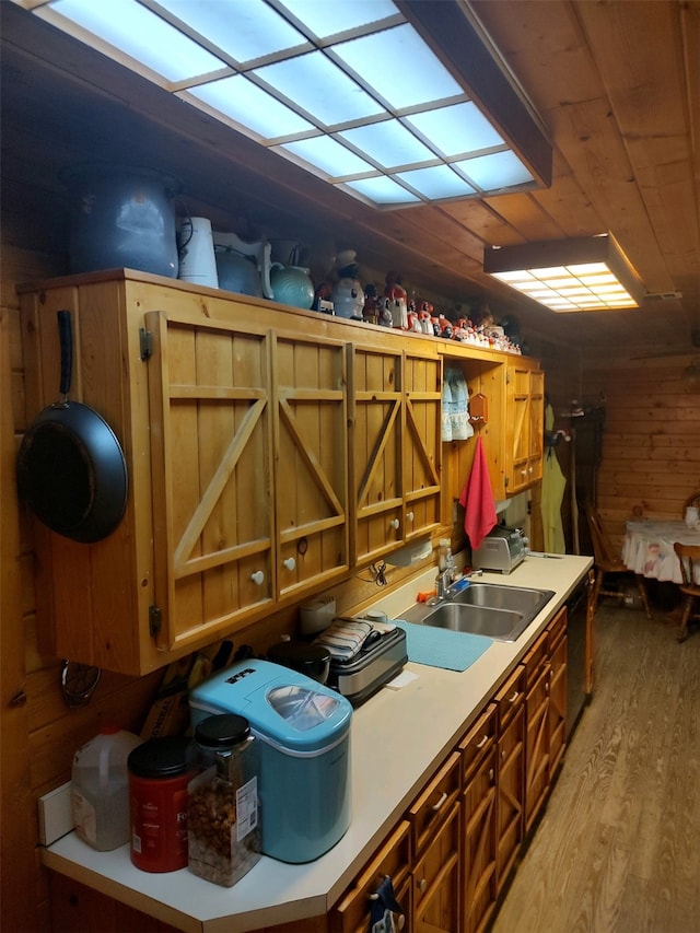 kitchen featuring wooden walls, sink, black dishwasher, and light wood-type flooring