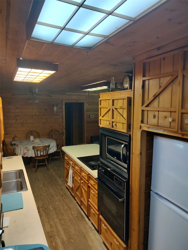 kitchen featuring wooden walls, sink, hardwood / wood-style floors, and black appliances