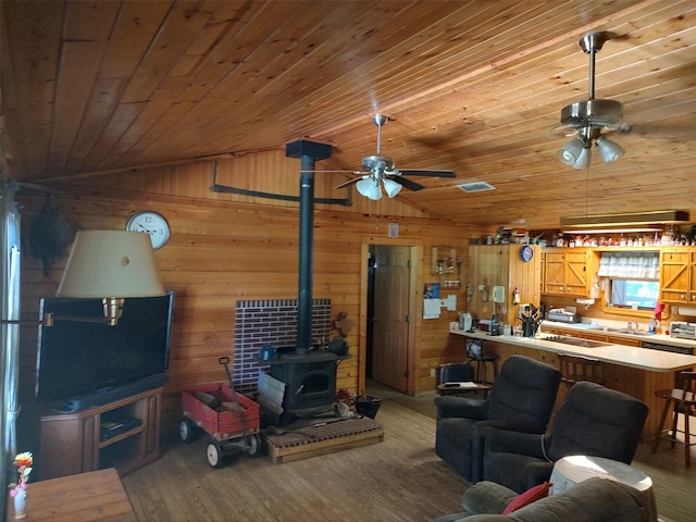 living room with hardwood / wood-style floors, a wood stove, wood walls, wood ceiling, and ceiling fan