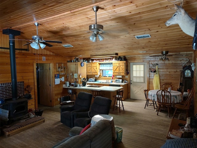 living room featuring ceiling fan, light hardwood / wood-style flooring, a wood stove, wood walls, and wooden ceiling