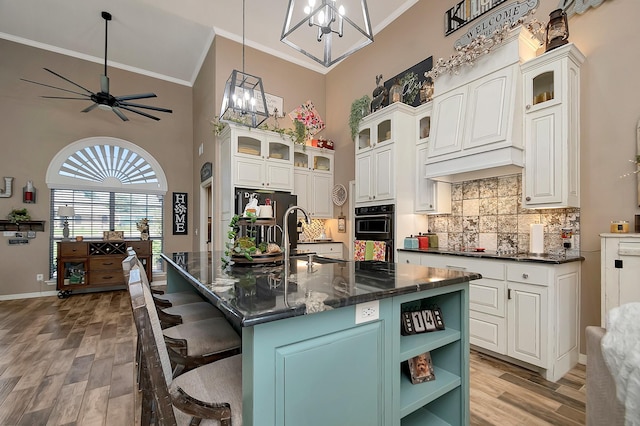 kitchen featuring a center island with sink, sink, ornamental molding, a kitchen bar, and white cabinetry