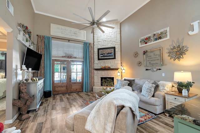 living room featuring a towering ceiling, hardwood / wood-style flooring, a stone fireplace, and ornamental molding