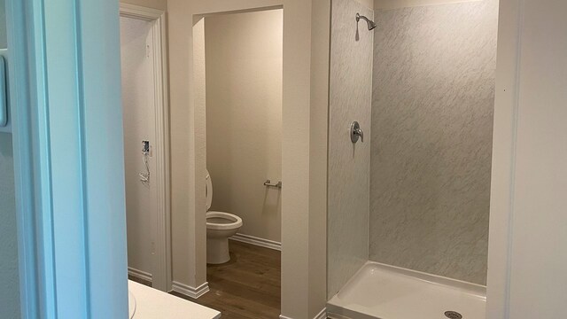 bathroom with tiled shower, toilet, and wood-type flooring