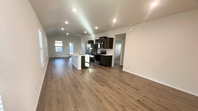 kitchen with wood-type flooring, stainless steel appliances, vaulted ceiling, and an island with sink