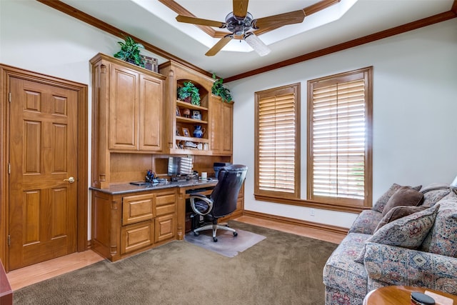 carpeted home office featuring ceiling fan, built in desk, and crown molding