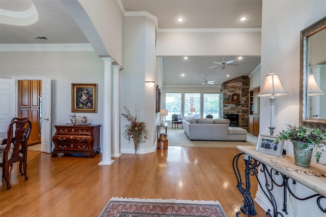 living room with ceiling fan, decorative columns, crown molding, a fireplace, and light wood-type flooring