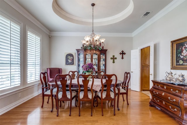 dining space featuring a chandelier, a raised ceiling, light hardwood / wood-style flooring, and ornamental molding