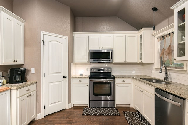 kitchen featuring lofted ceiling, light stone counters, sink, backsplash, and appliances with stainless steel finishes