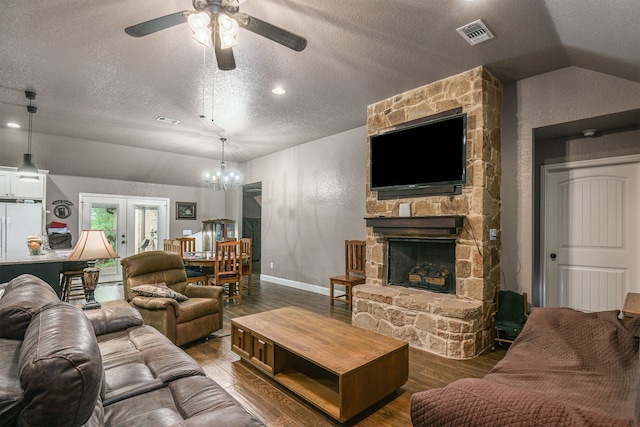 living room with a stone fireplace, ceiling fan with notable chandelier, lofted ceiling, hardwood / wood-style floors, and a textured ceiling