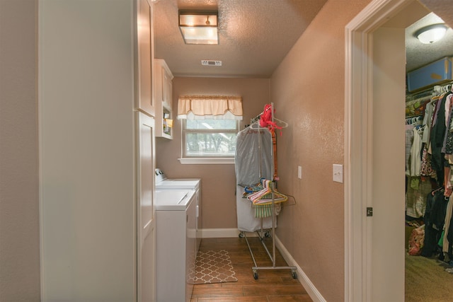 clothes washing area with washer and clothes dryer, cabinets, wood-type flooring, and a textured ceiling