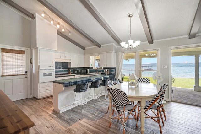 dining area featuring vaulted ceiling with beams, light hardwood / wood-style flooring, a water view, and a chandelier