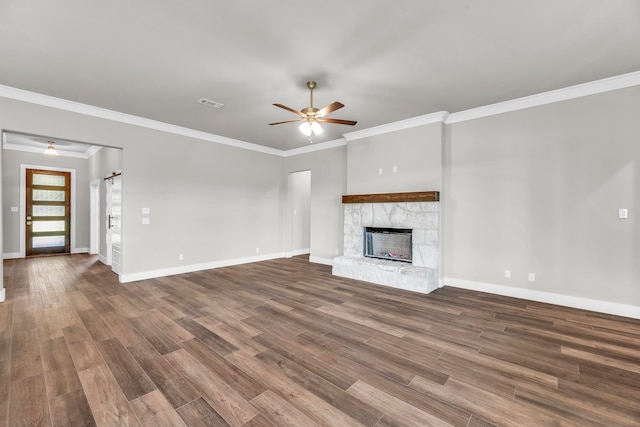 unfurnished living room featuring a barn door, a stone fireplace, wood-type flooring, and ornamental molding