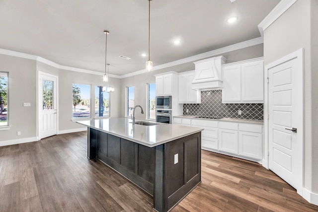 kitchen with custom exhaust hood, a center island with sink, sink, white cabinetry, and stainless steel appliances