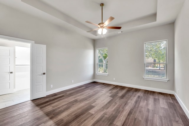 empty room featuring hardwood / wood-style flooring, ceiling fan, a wealth of natural light, and a tray ceiling