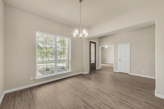 empty room with a notable chandelier, a wealth of natural light, and dark wood-type flooring