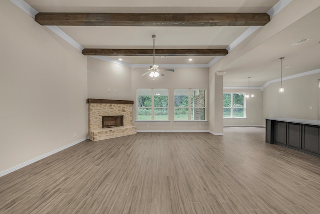 unfurnished living room featuring a fireplace, beamed ceiling, light wood-type flooring, crown molding, and ceiling fan