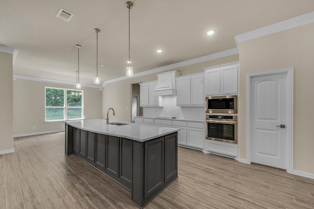 kitchen featuring appliances with stainless steel finishes, white cabinets, light wood-type flooring, a kitchen island with sink, and sink