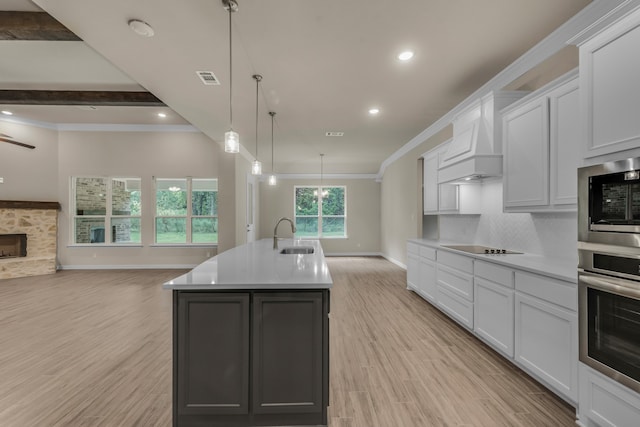 kitchen featuring an island with sink, white cabinets, oven, decorative light fixtures, and a stone fireplace