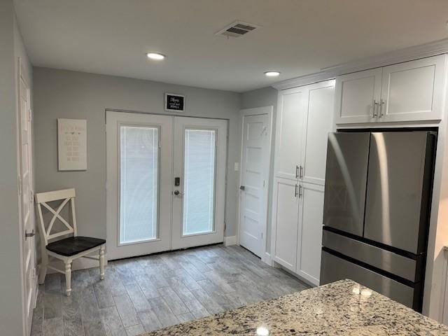 kitchen featuring light stone countertops, white cabinets, french doors, light hardwood / wood-style floors, and stainless steel refrigerator