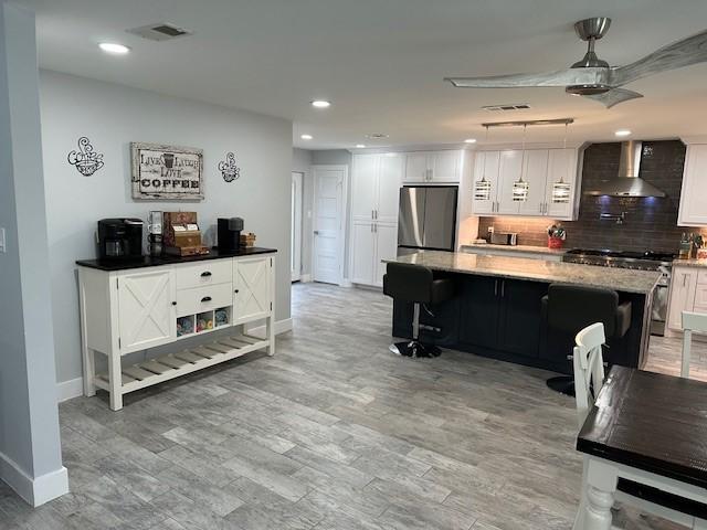 kitchen with a spacious island, pendant lighting, appliances with stainless steel finishes, wall chimney range hood, and white cabinetry