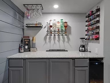 bar featuring light stone counters, wooden walls, and gray cabinets