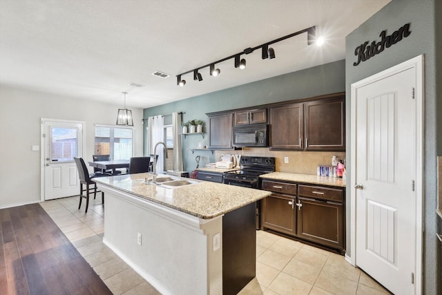 kitchen featuring pendant lighting, sink, a kitchen island with sink, black appliances, and dark brown cabinetry