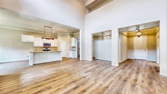 unfurnished living room with a towering ceiling, crown molding, and light hardwood / wood-style flooring