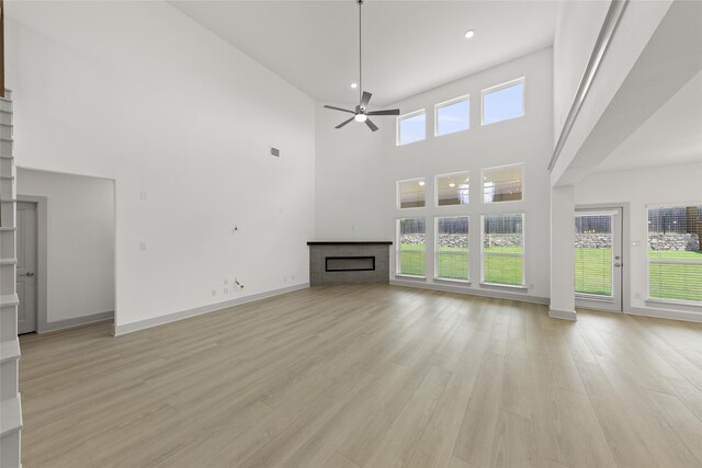 unfurnished living room with light hardwood / wood-style floors, a fireplace, ceiling fan, and a high ceiling