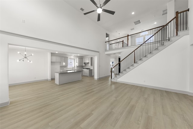 unfurnished living room with light hardwood / wood-style floors, ceiling fan with notable chandelier, and high vaulted ceiling