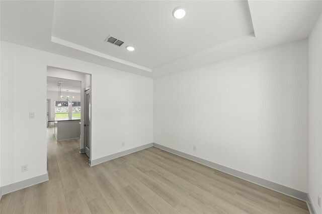 unfurnished room featuring a chandelier, light wood-type flooring, and a raised ceiling