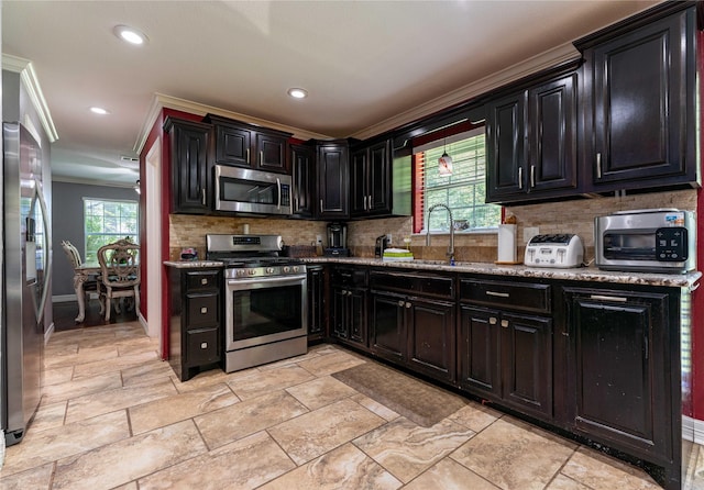 kitchen with backsplash, sink, light stone countertops, appliances with stainless steel finishes, and ornamental molding