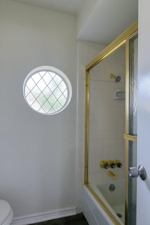 bathroom featuring shower / bath combination with glass door and toilet