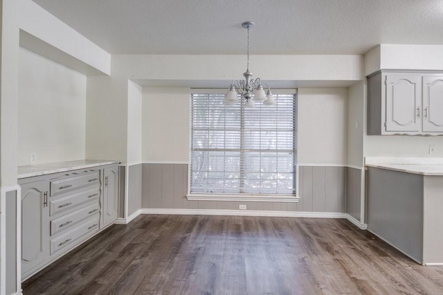 unfurnished dining area featuring a textured ceiling, a chandelier, and dark hardwood / wood-style floors