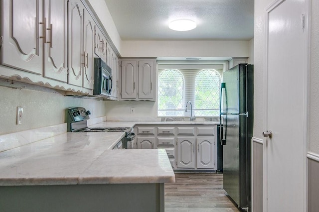 kitchen with black appliances, light wood-type flooring, kitchen peninsula, and gray cabinets