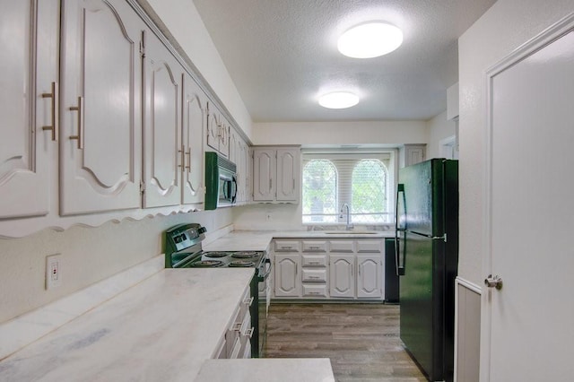 kitchen with black appliances, light wood-type flooring, a textured ceiling, and sink