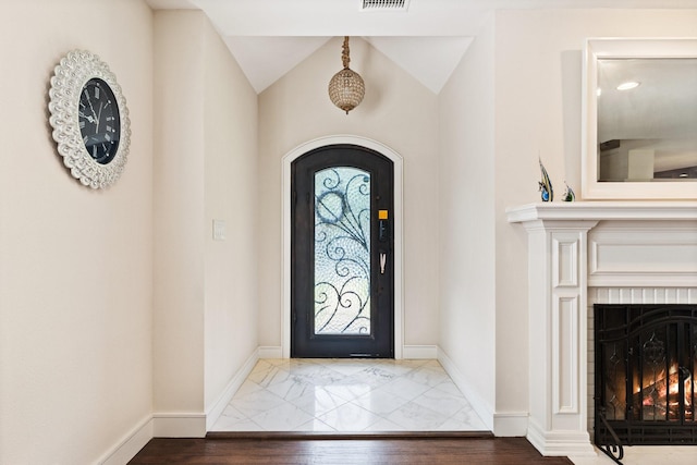 foyer entrance with a tile fireplace and vaulted ceiling