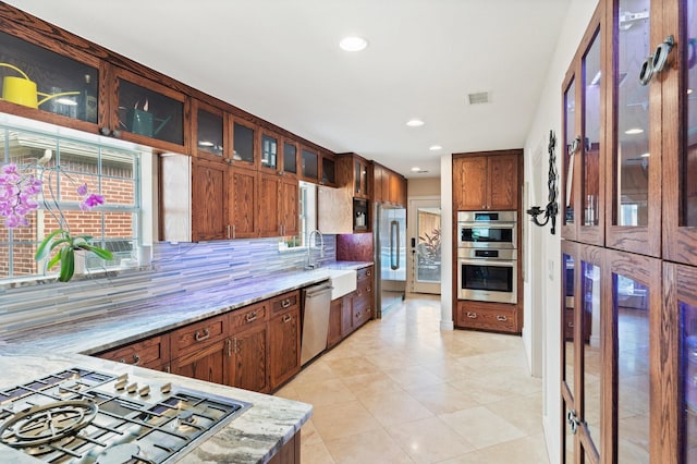 kitchen featuring sink, decorative backsplash, light tile patterned floors, light stone countertops, and appliances with stainless steel finishes