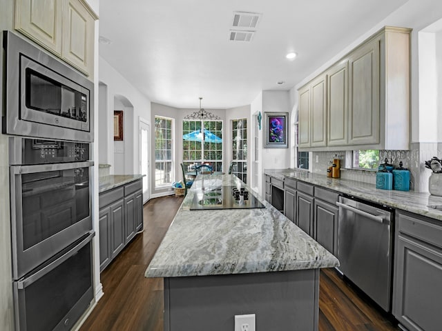 kitchen featuring a center island, light stone counters, dark hardwood / wood-style floors, backsplash, and appliances with stainless steel finishes