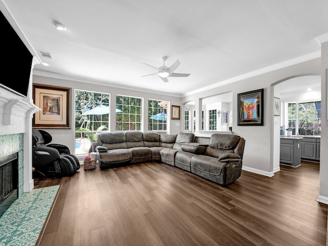 living room with dark hardwood / wood-style floors, ceiling fan, crown molding, and a tiled fireplace