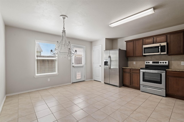 kitchen with appliances with stainless steel finishes, backsplash, hanging light fixtures, light stone countertops, and dark brown cabinets