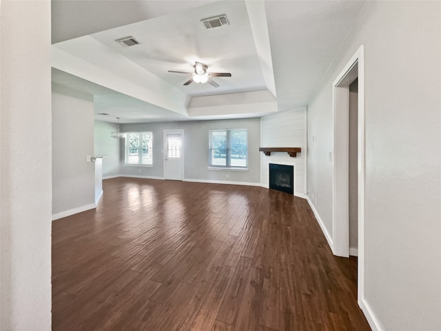 unfurnished living room with a raised ceiling, ceiling fan with notable chandelier, and dark hardwood / wood-style flooring