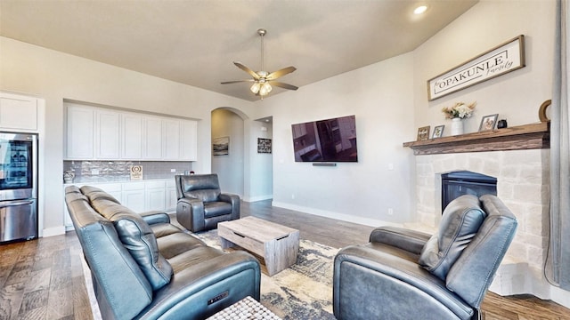 living room featuring a stone fireplace, ceiling fan, and dark hardwood / wood-style floors